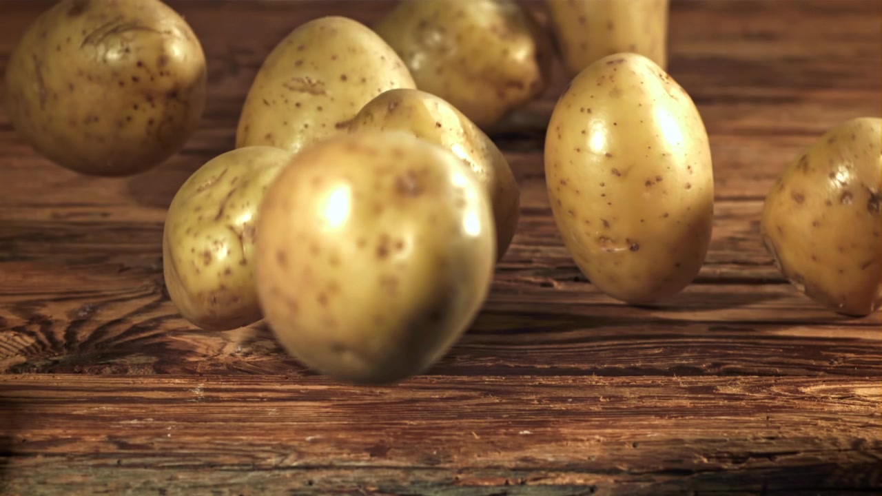 Patate fresche crude che cadono e rotolano su un tavolo di legno rustico