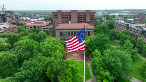 aerial orbit around waving american flag on university of michigan campus on rainy summer day