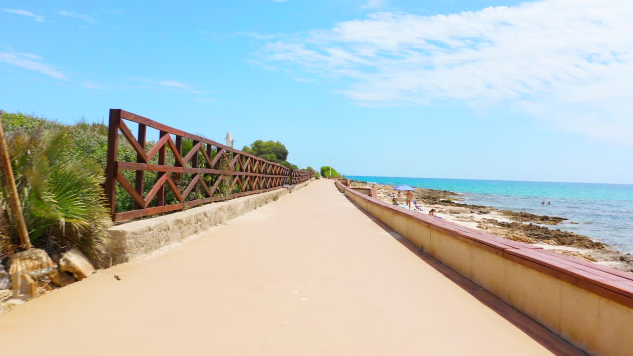 POV walking along beautiful beautiful beach promenade with crystal clear blue water and coastline in Spain, Europe
