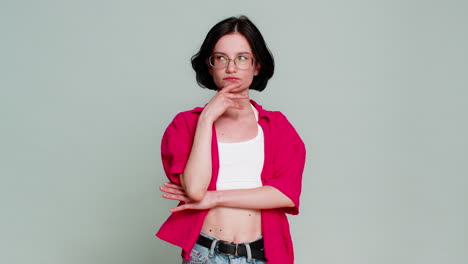 Young woman smiles suddenly raises finger up after thinking moment showing eureka idea inspiration