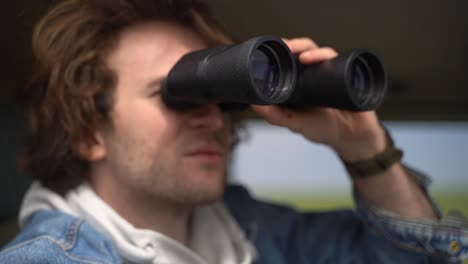 young boy looks with a pair of binoculars from a car.