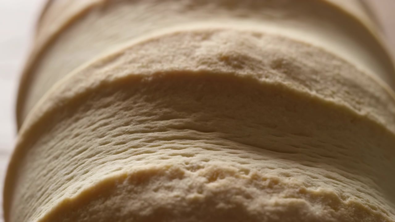 Low-angle close detail of stacked round tortillas or flatbreads, showing repeating curved edges, porous dough texture, warm beige tones, soft shadows, and simple rustic food presentation