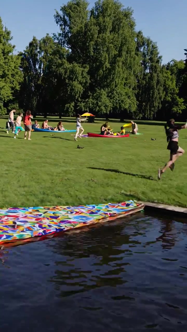 Unga människor som springer och hoppar ner i en sjö i en park