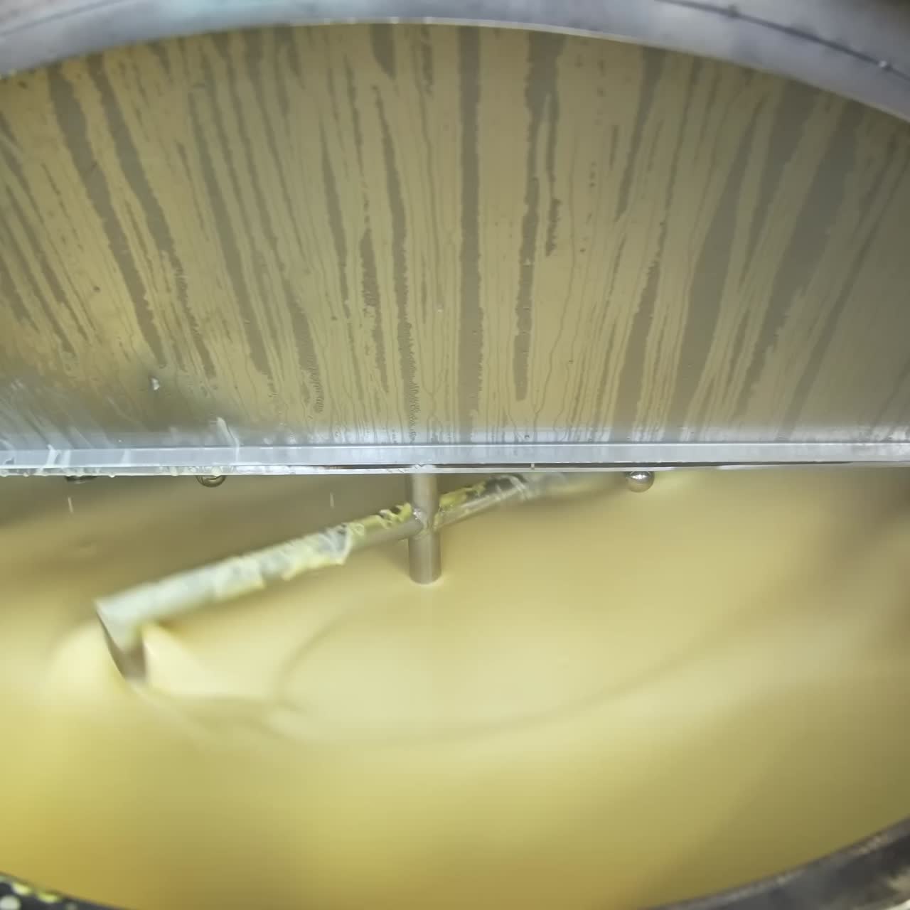 Automatic mixing of milk cream inside large industrial stainless steel reservoir. Large tanks for storing and fermenting dairy products. Close up