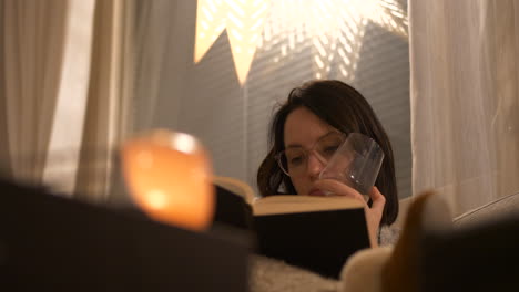 Woman-with-glasses-reading-book-in-living-room-sofa,-Christmas-time-season,-sliding-left