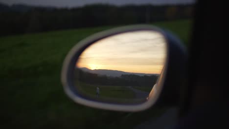 backview of a car mirror with beautiful scenery landscape at sunset with fields