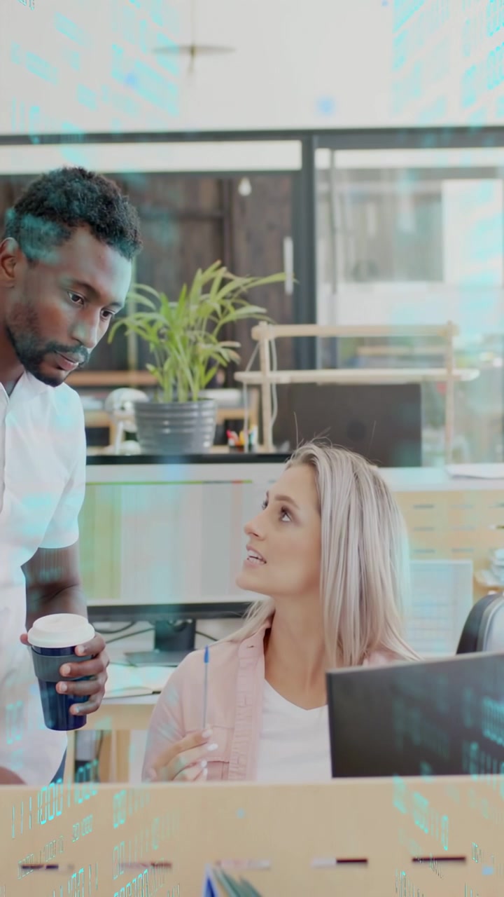Vertical video: Standing man leaning in causing seated woman reviewing PC with pen, cup for work