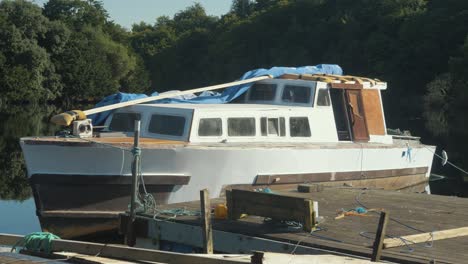 Old-liveaboard-boat-painted-white-being-repaired-while-moored-to-pier-on-lake