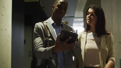 diverse businessman and businesswoman talking and using tablet in corridor of modern office