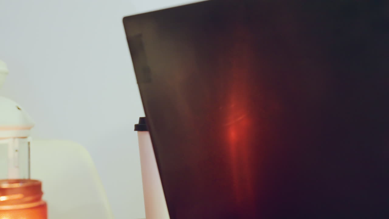 Kaukasischer Mann konzentriert sich mit aufmerksamem Ausdruck auf das Leuchten des Laptop-Bildschirms, trinkt aus einer Tasse, Laternenlicht und reflektierender Monitor, tippt und liest Code oder Notizen während einer späten Lernsitzung, konzentriert