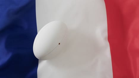 White-rugby-ball-over-waving-flag-of-france-with-copy-space,-in-slow-motion