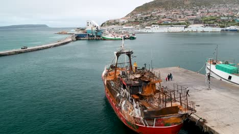 un dron vuela sobre un barco de pesca viejo y oxidado que está atracado en un puerto
