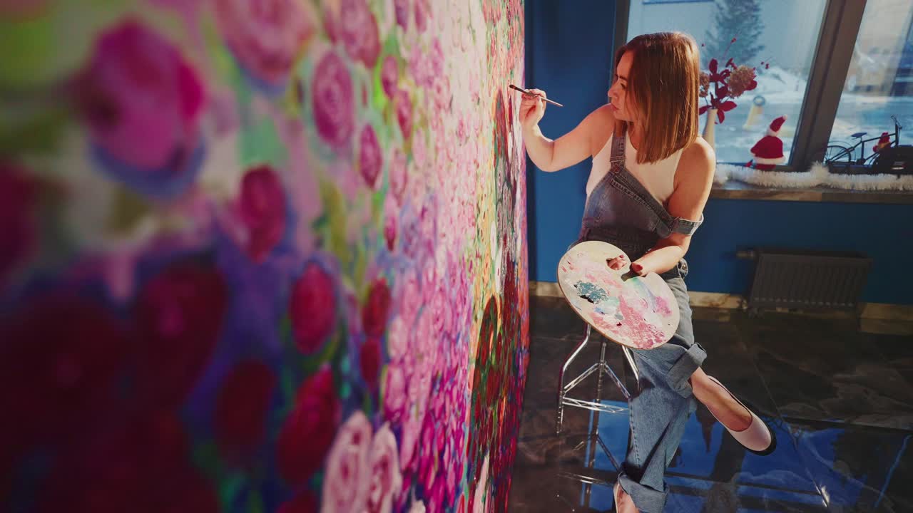 Joven mujer artista pintando un gran lienzo floral en su estudio