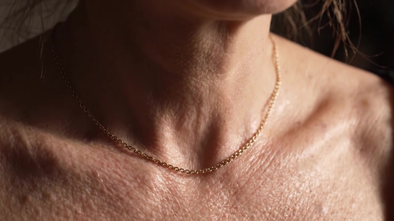 Un primo piano accattivante di una delicata collana d'oro sulla pelle, che enfatizza la texture e l'eleganza in un'ambientazione delicatamente illuminata