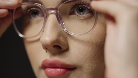 close up tilt up of a young pretty woman putting on glasses as a visual aid for better vision to see more clearly with better eyesight in slow motion against black background