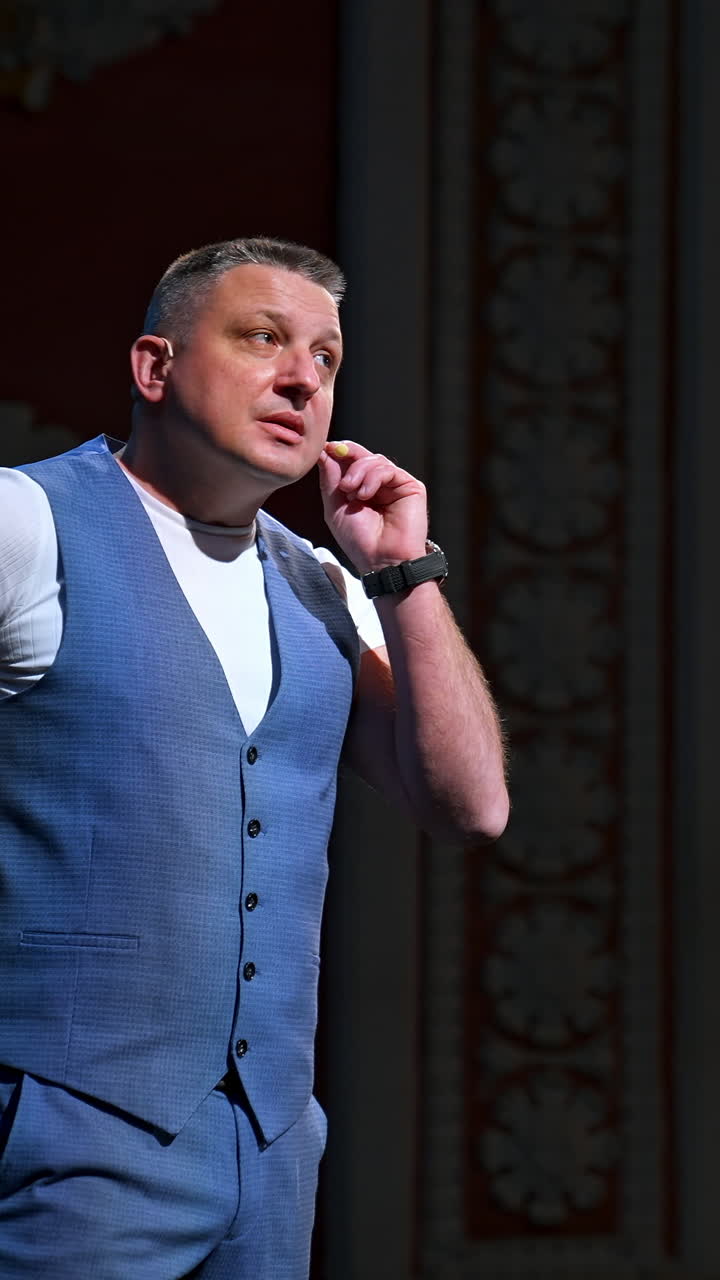 Host in grey suit on stage. Male actor starts his performance in the theater. Portrait of a comedian standing on stage and talking. Vertical video