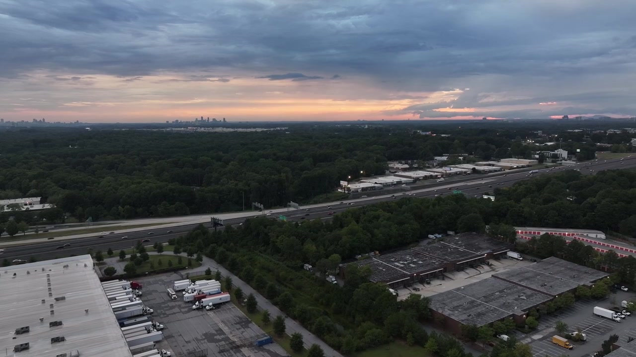 Ripresa con drone della strada statale Interstate 285 con magazzini industriali in vista al tramonto, distretto commerciale di North Atlanta, USA.