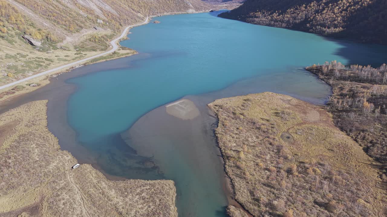 A drone-filmed view of a glacial lake with striking turquoise-green waters in Norway, surrounded by autumn mountains. Jotunheimen
