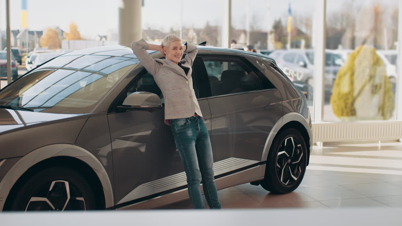 쇼 에 있는 새로운 전기 자동차 에 기대어 있는 행복 한 여자