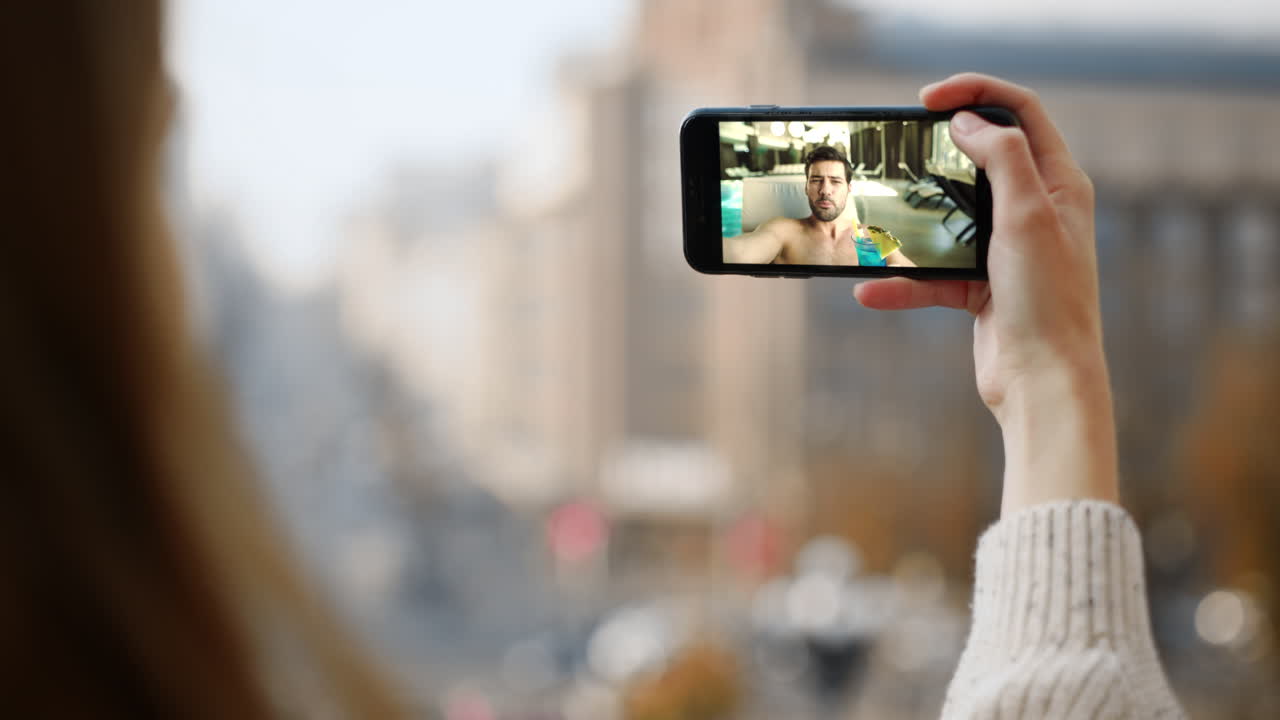 Homem distante falando com uma mulher em uma conferência on-line. Close-up de uma mão segurando um smartphone