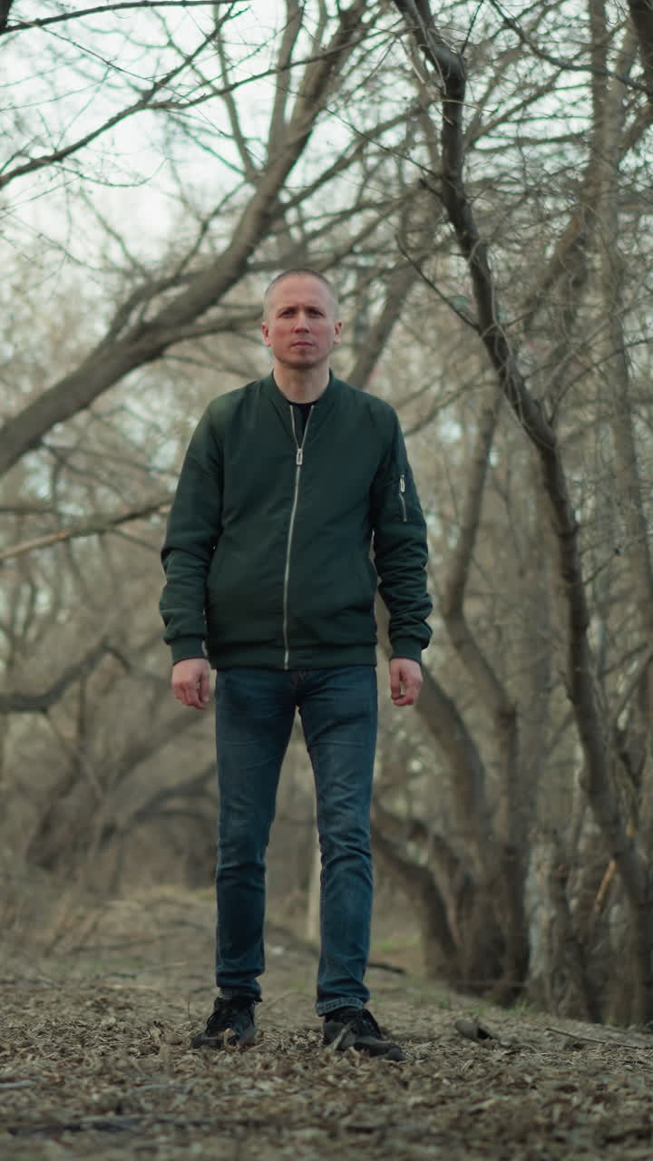 un hombre camina a través de un denso bosque con árboles desnudos a principios de la primavera, con una chaqueta negra, pantalones vaqueros y lona