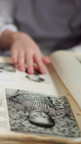 little child palm hides and strokes picture of grandmother in old family photo album sitting with father on couch close view slow motion