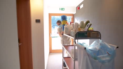 housekeeping lady with face mask and the floor trolley walks through a corridor in the hotel