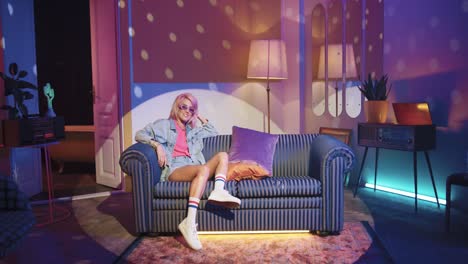 young beautiful woman in stylish clothes sitting on sofa in a retro party at home