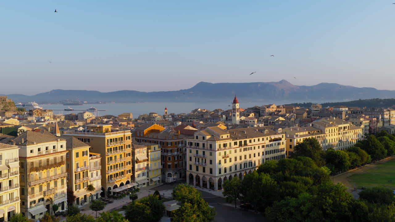 Establishing drone shot of Old town of Corfu during sunrise on Ionian Sea with flock of birds taking flight above town