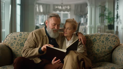 Smiling-old-couple-looking-photo-album-in-the-living-room