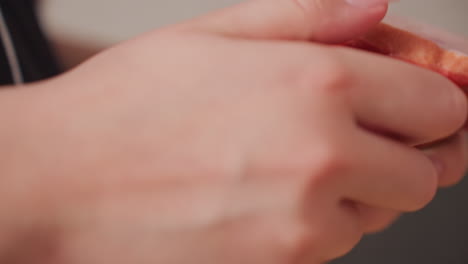 extreme close up view of hand peeling plastic wrapper from red hotdog surface showing detail of packaging removal during food preparation with visible texture of meat