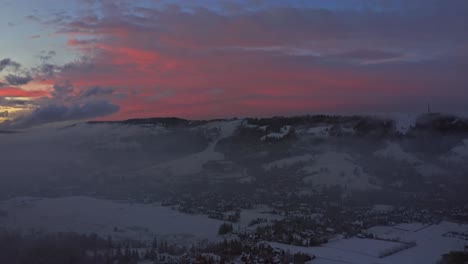 puesta de sol roja ardiente sobre la ciudad rural de zakopane con niebla dramática en el valle, antena