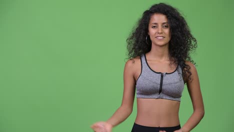 young beautiful hispanic woman with gym clothes showing something