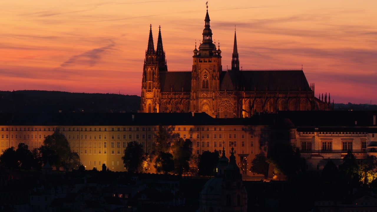 Veduta aerea con drone del Castello di Praga illuminato e della Cattedrale di San Vito che risplendono contro un vivido cielo al tramonto arancione e rosa, Praga, Repubblica Ceca.