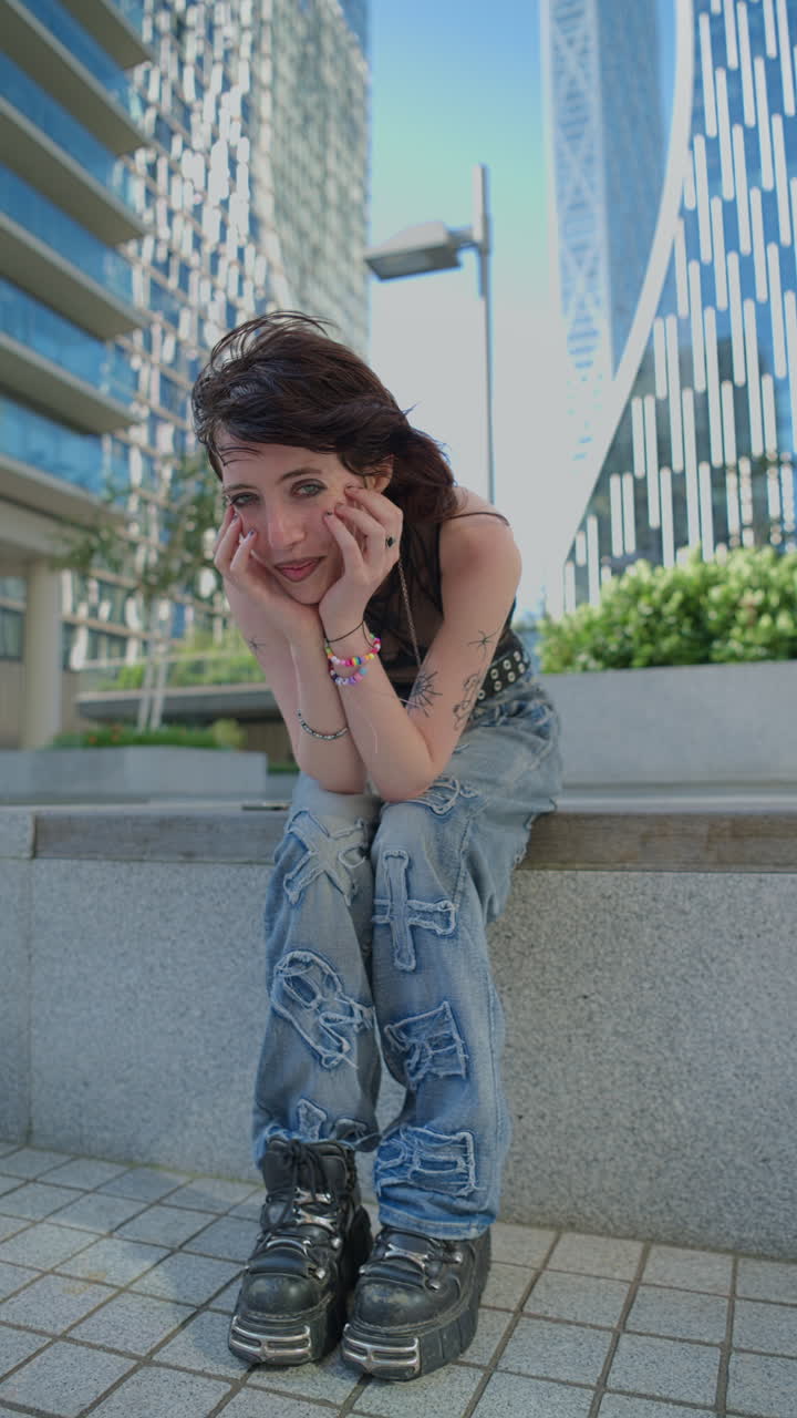 vídeo vertical de moda al aire libre retrato de una joven sonriente de estilo alternativo mujer con tatuajes y perforaciones sentada fuera de edificios modernos en canary wharf londres disparado en tiempo real