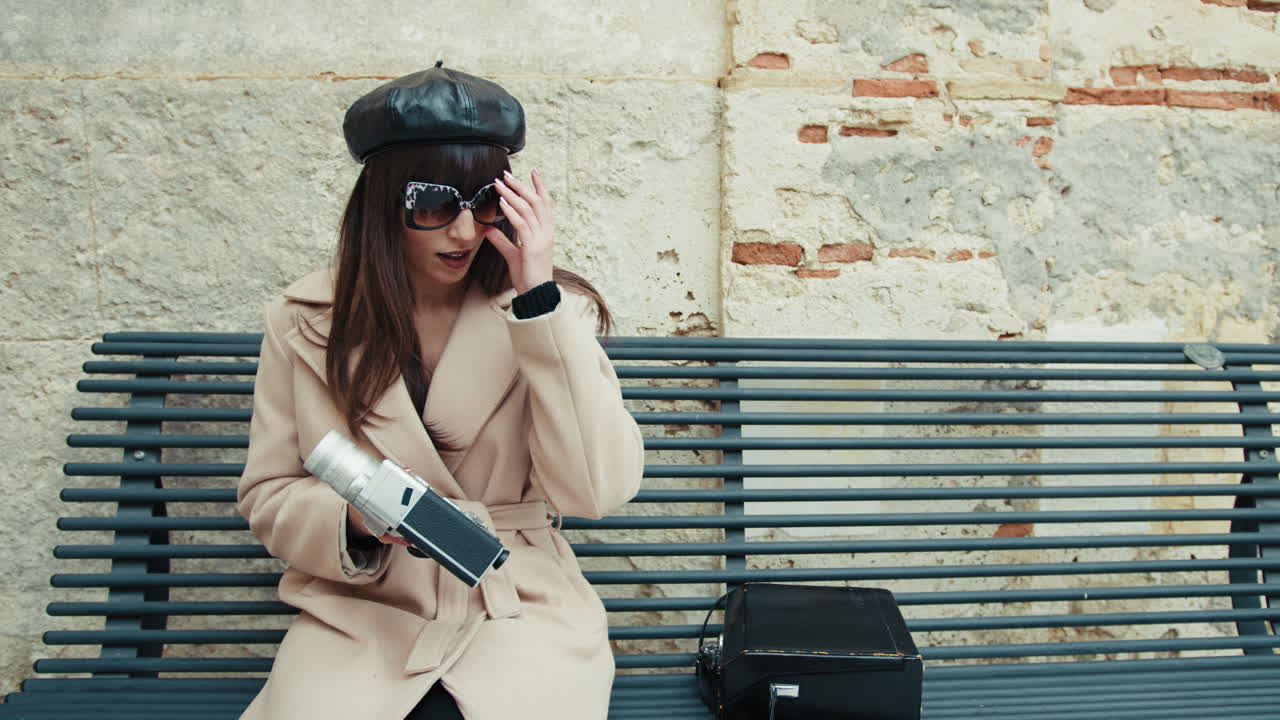Happy Woman With A French Hat Picking Up A Vintage Camera While On A Bench