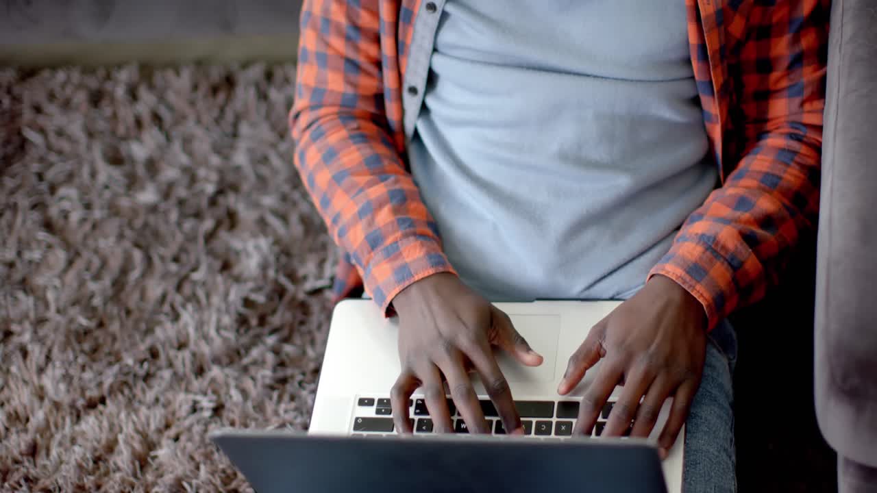 Happy african american man sitting on floor using laptop at home, slow motion