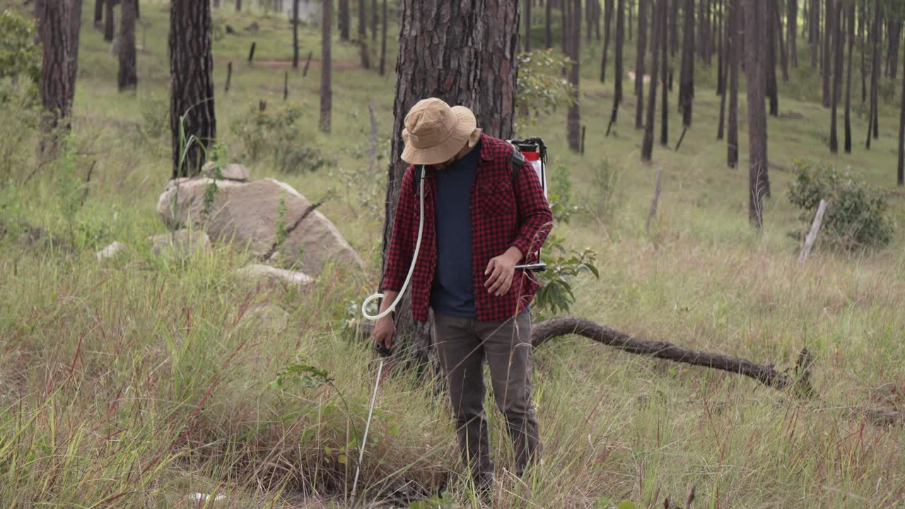 숲에서 배 ⁇  스프레이어와 함께 일하는 남자의 넓은  ⁇ , 그는 빨간 셔츠와 모자를 입고 있습니다