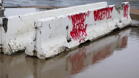 Static-shot-of-an-old-concrete-jersey-barrier-with-red-graffiti-on-it-during-a-rainy-day