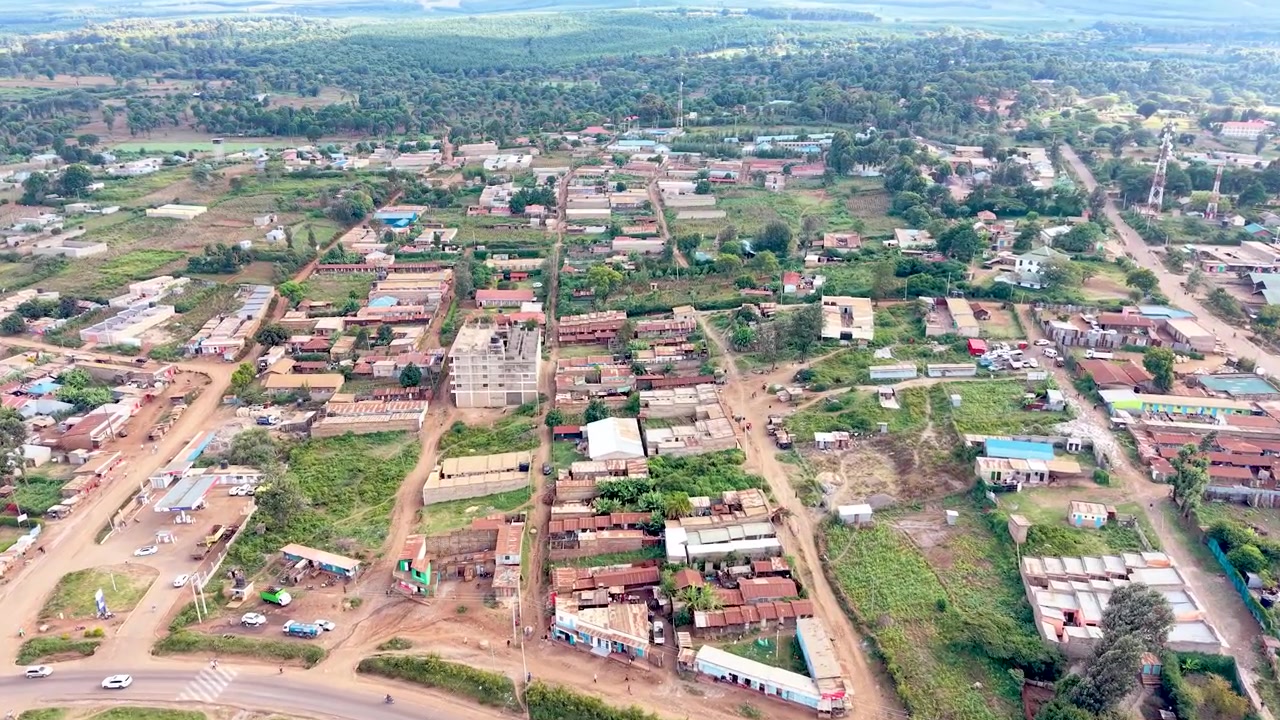 Una vista cinematografica del Kenya rurale che mostra insediamenti informali con tetti di lamiera arrugginiti, case logore, sentieri polverosi del villaggio e la vita quotidiana della comunità.