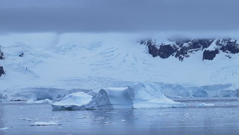 Iceberg-Y-Montañas-Invernales-En-Un-Paisaje-Azul-Frío-En-La-Antártida-Con-Hielo-Y-Glaciar-En-Una-Espectacular-Y-Hermosa-Escena-Costera-En-La-Costa-De-La-Península-Antártica,-Atmósfera-Azul-Cambiante