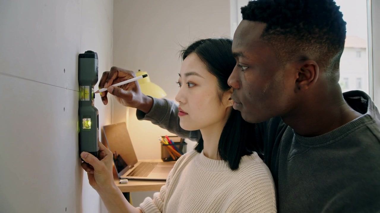 Pressing stud finder, man guiding woman cream sweater marking wall to mount at home with pencil