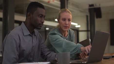 diverse male and female business colleagues in discussion at work using laptop and tablet