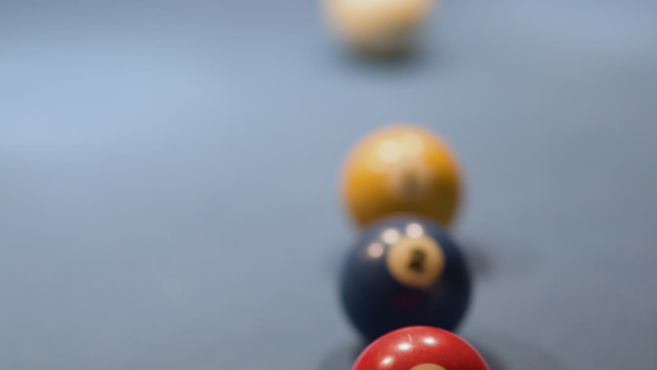 Billiard balls roll in sequence toward a corner pocket on blue felt under low light