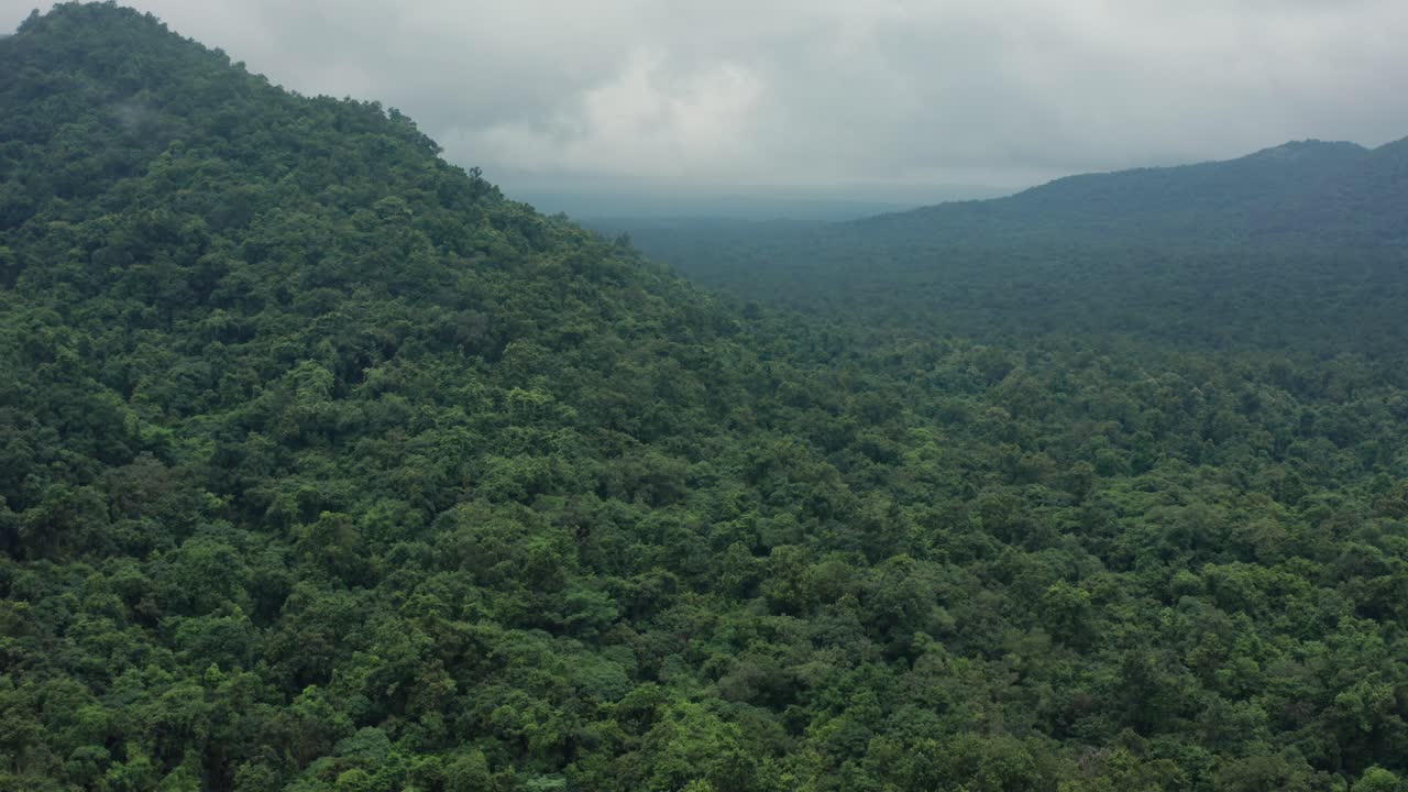Vaste présentation aérienne d’une vallée verdoyante et boisée, bordée de pentes voilées de brume et de pics lointains à Kuldiha sous un ciel nuageux, évoquant les profondeurs d’un sanctuaire sauvage
