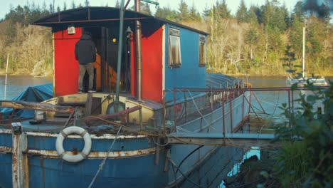 young man living on barge houseboat carrying logs enters wheelhouse