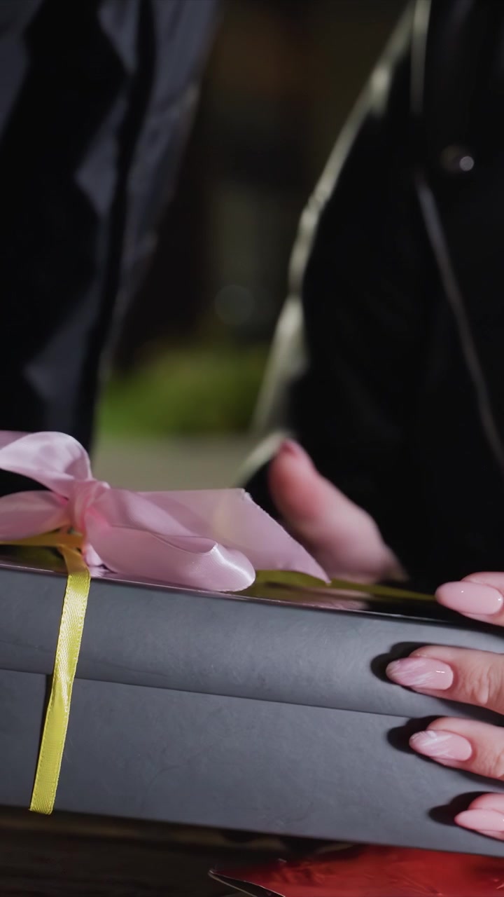 Un lettore interagisce con una pubblicazione aperta alla luce. Un libro rosso è appoggiato sul tavolo mentre le mani sistemano oggetti vicini. Un tavolo di legno è parzialmente visibile sotto le mani del soggetto di notte.