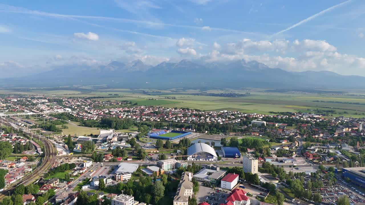 Drone rising above Poprad and flying forward, revealing the city and the High Tatras in the distance on a sunny day