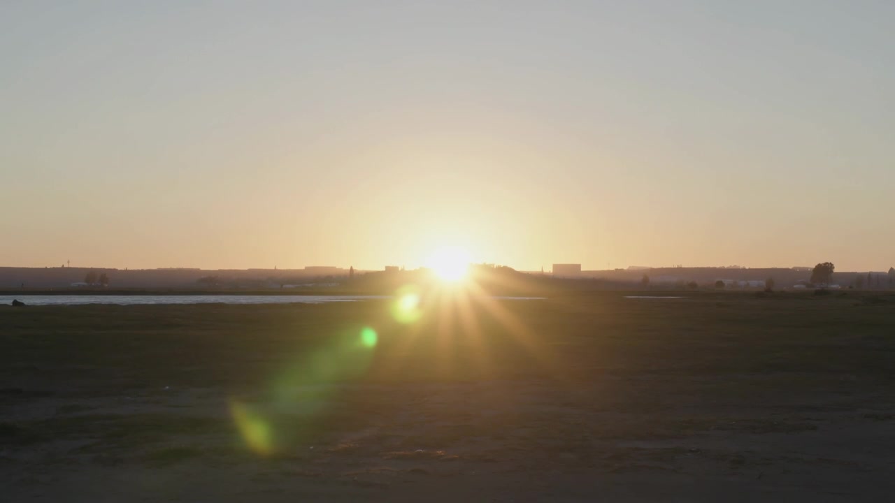 Peeking sun above ridge at dawn casting starburst rays, producing green lens flare on water channel