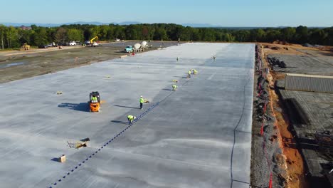 workers insert bolts into concrete to separate panels while concrete trucks pour concrete